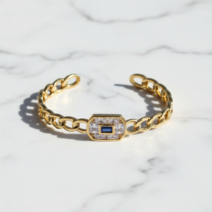 Gold bracelet with a central gemstone on a marble background