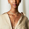 A woman wearing a gold-filled necklace with leaf-shaped pendants and a beaded chain.