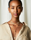 A woman wearing a gold-filled necklace with leaf-shaped pendants and a beaded chain.