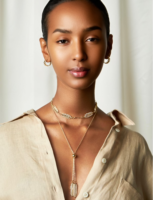 A woman wearing a gold-filled necklace with leaf-shaped pendants and a beaded chain.