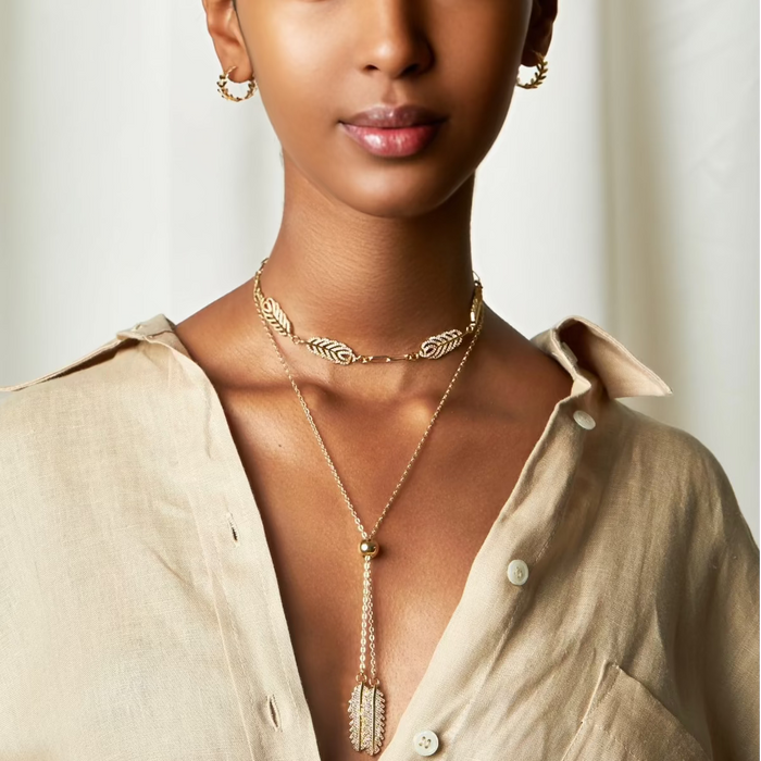A woman wearing a gold-filled necklace with leaf-shaped pendants and a beaded chain.