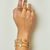 Hand wearing multiple gold rings and bracelets on a light background