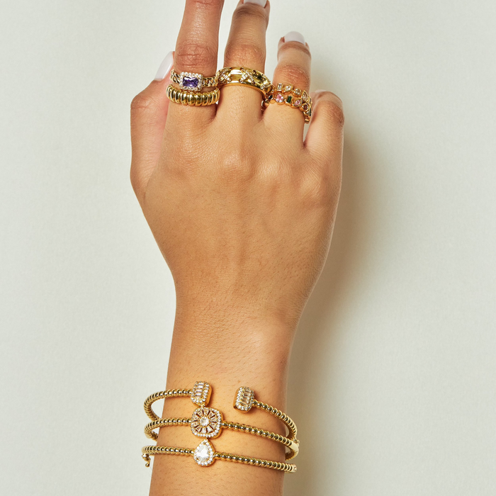 Hand wearing multiple gold rings and bracelets on a light background