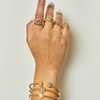 Hand wearing multiple gold rings and bracelets on a plain background