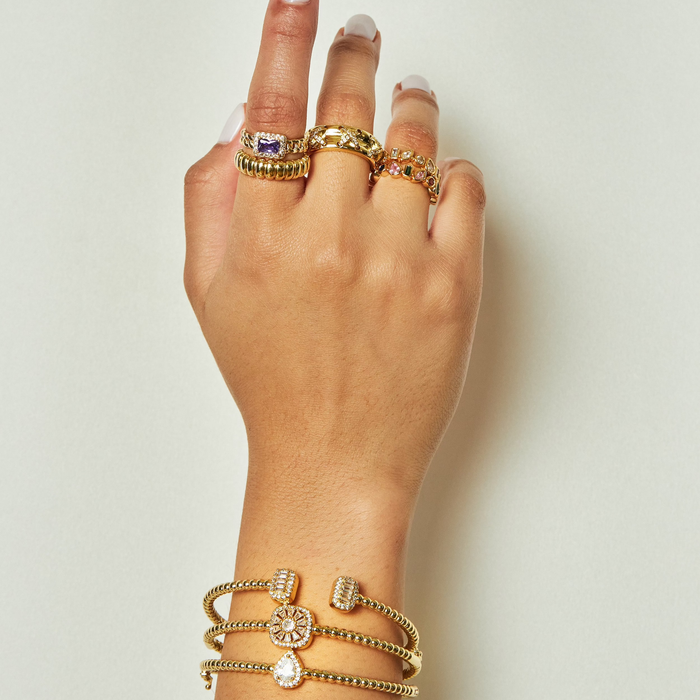 Hand wearing multiple gold rings and bracelets on a plain background