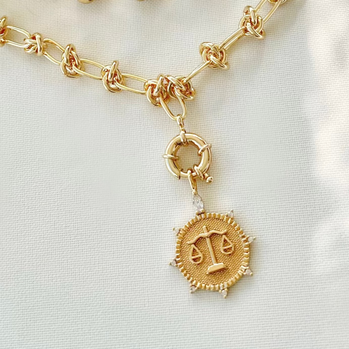 A gold-filled necklace with a zodiac pendant featuring a circular chain link design and a gold-tone pendant.