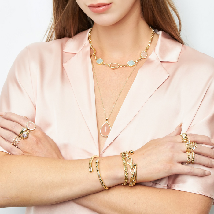 Woman wearing gold jewelry including necklaces, bracelets, and rings on a white background