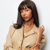 Woman wearing a beige jacket with gold jewelry against a white background