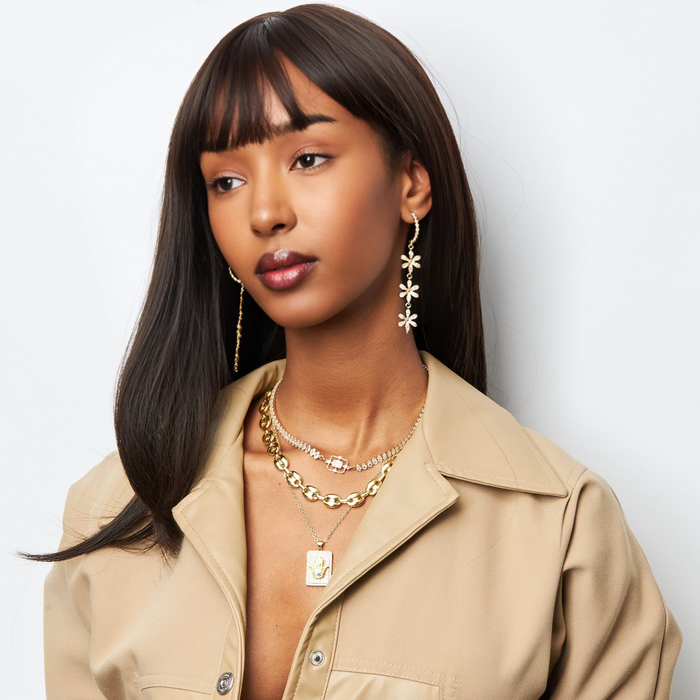 Woman wearing a beige trench coat with gold jewelry against a light background