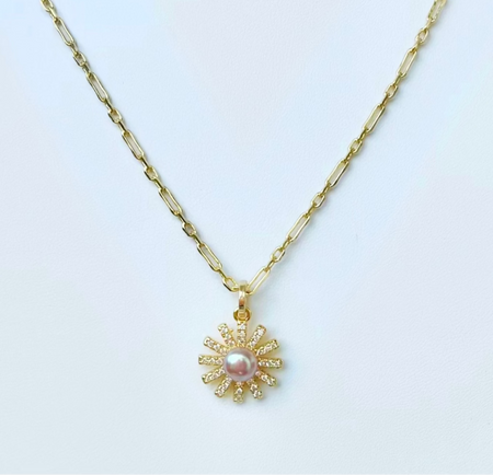 Gold necklace with a sunflower pendant on a light gray background