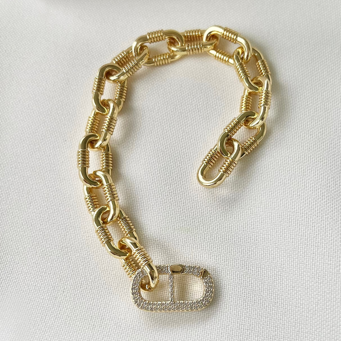 A gold filled chunky chain link bracelet with a large clear crystal micro pave diamond connector, displayed on a white surface.