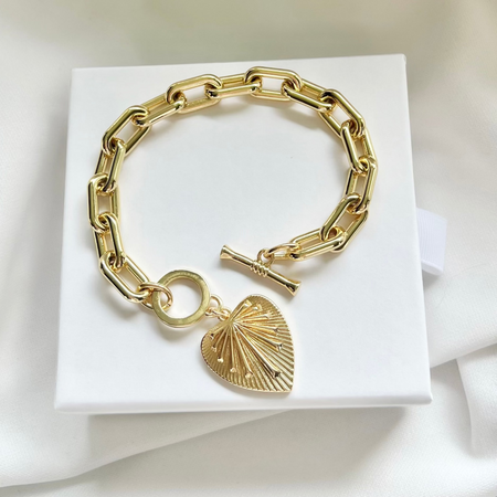 A gold-filled chain link bracelet with a heart pendant and a toggle clasp, presented on a white surface.