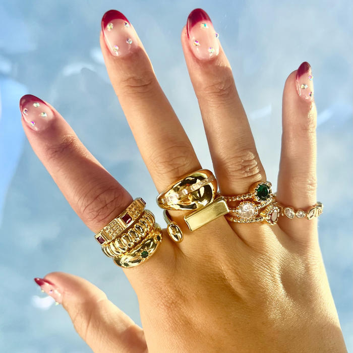 Hand wearing multiple gold rings with a blurred blue background