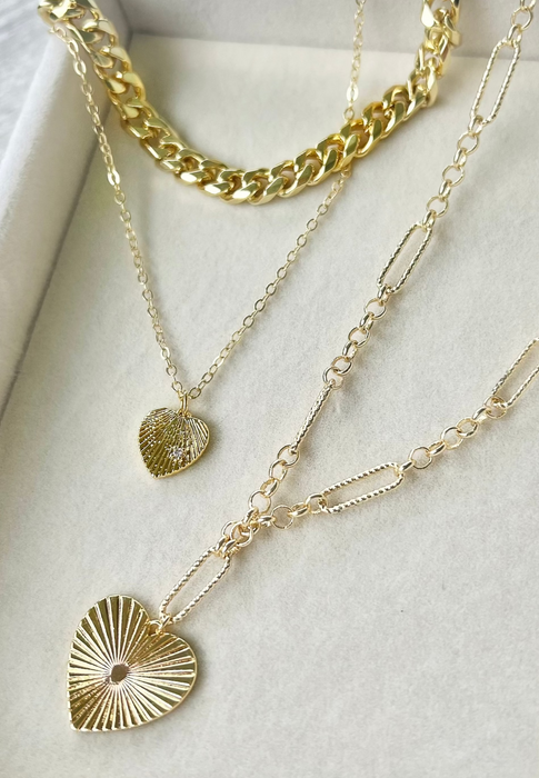Three gold necklaces with heart-shaped pendants on a white surface