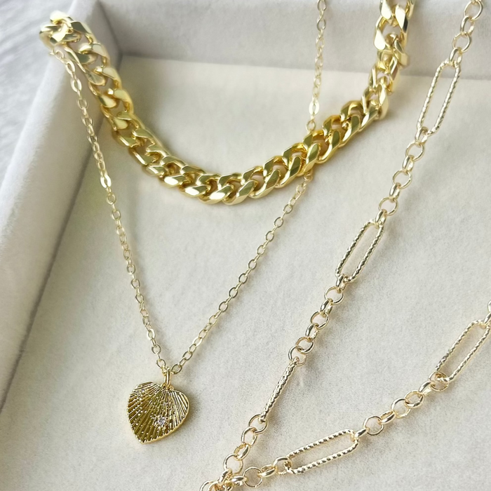 Three gold necklaces with heart-shaped pendants on a white surface
