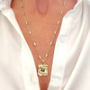 A gold-filled necklace with a hammered pendant featuring a blue stone, worn by a person with a white shirt.