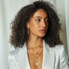 Woman wearing a white blazer and multiple necklaces with a neutral background