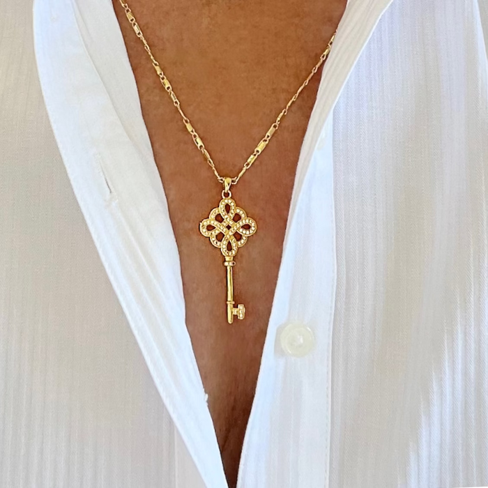 A gold-filled necklace with a pendant in the shape of a key, featuring intricate details and adorned with cz diamonds and micro pave crystals, displayed on a person.