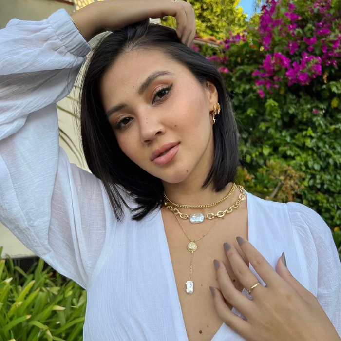 A woman wearing a white sleeveless top and gold-filled necklaces with freshwater pearl connectors.