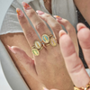 A person's hand showcasing multiple gold-filled rings with colorful gemstones and micro pave crystals.
