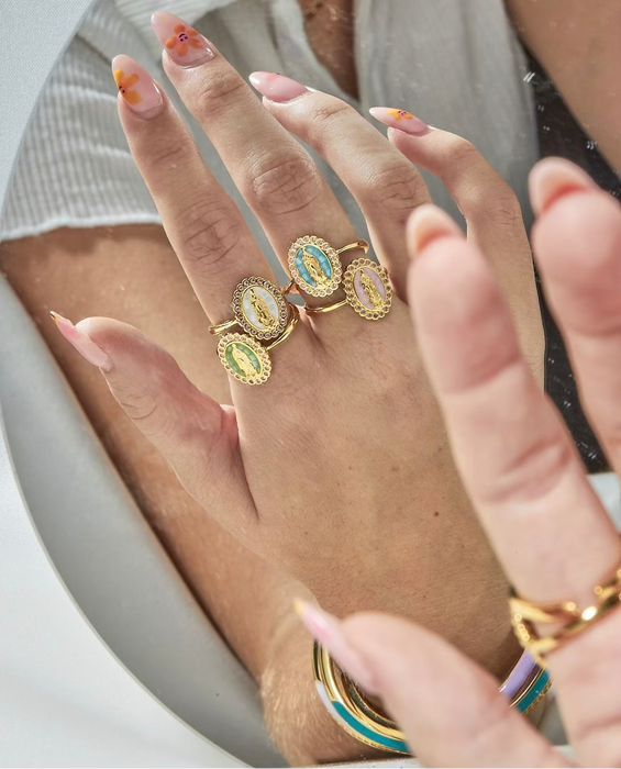 A person's hand showcasing multiple gold-filled rings with colorful gemstones and micro pave crystals.