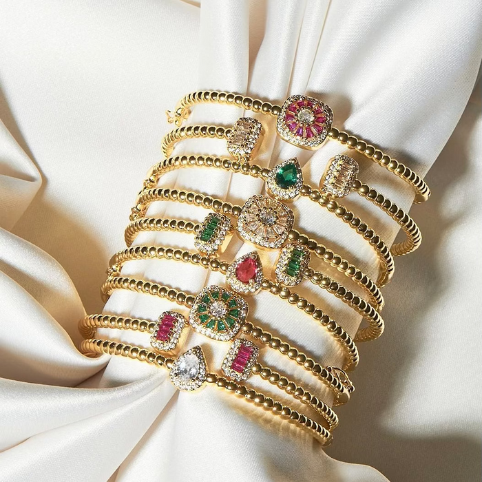 Set of gold bracelets with gemstones on a white fabric background